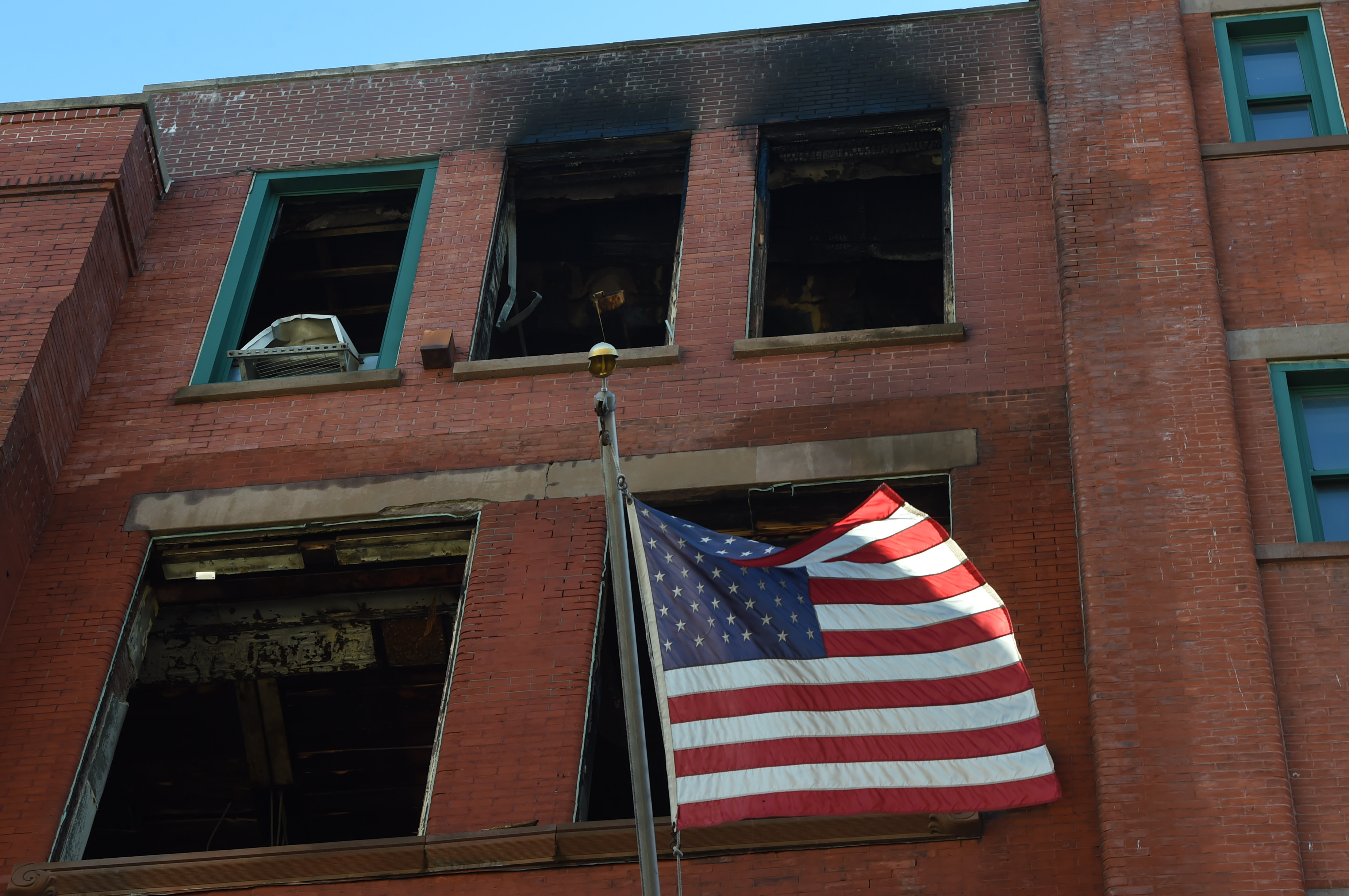 A flag still waves out front of the burned out building. 