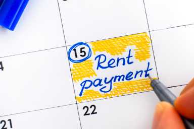 Woman fingers with pen writing reminder Rent Payment in calendar.