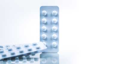 Colchicine 0.6 mg tablets pills in light resistant packaging isolated on white background. Gout attack, gout pain and gouty arthritis concept. Pharmaceutical industry. Pile of white blister pack.