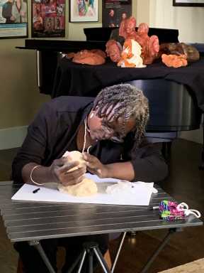 Joyce bending over work with clays in bg – great shot