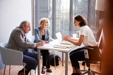 Senior Couple Signing Document In Meeting With Female Financial Advisor In Office