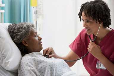 African nurse using stethoscope on hospital patient