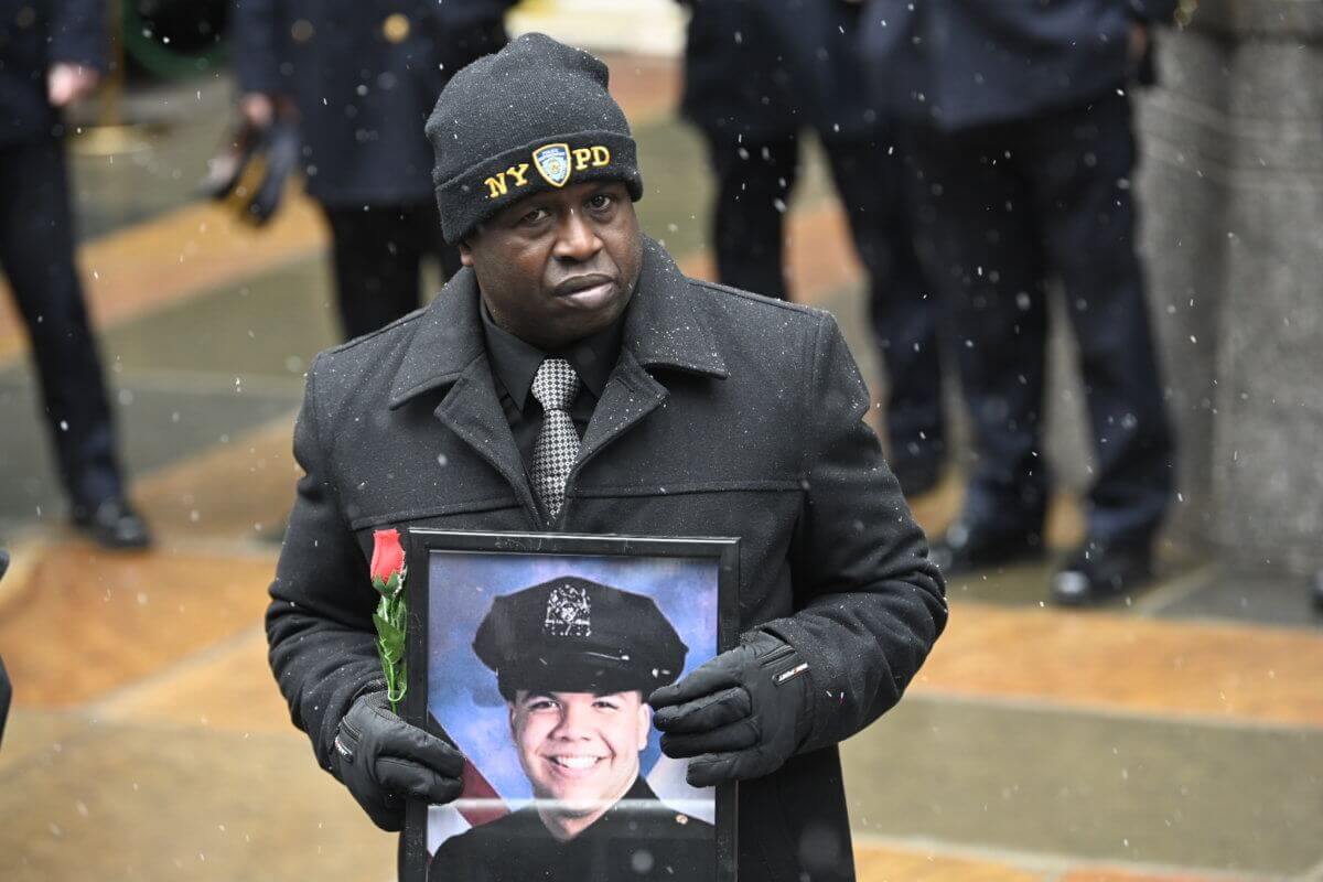 A man carries a photograph of slain Police Officer Jason Rivera alongside a rose