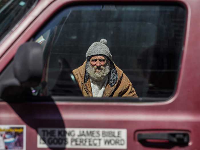 A homeless man looks through a window of a van from a street in Midtown.