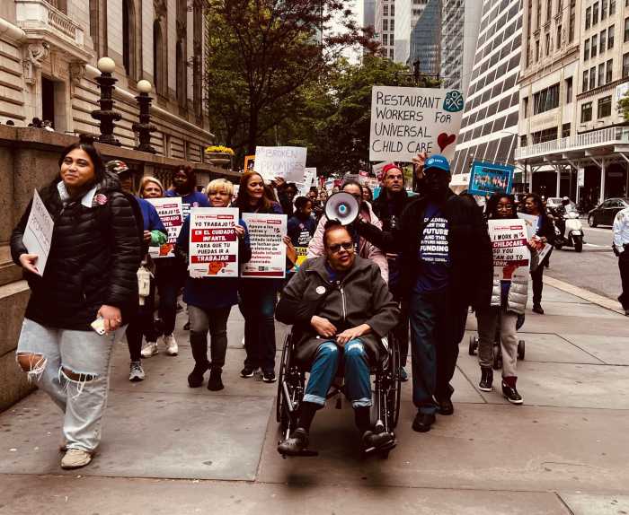 people marching on a side walk in Manhattan holding signs to support child care funding