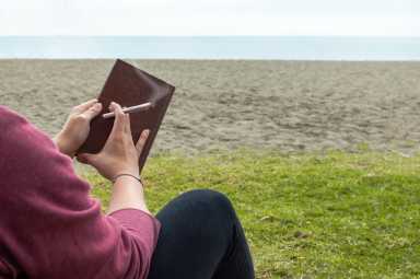 Housing Works Cannabis Co's Weed & Read program pairs cannabis products with good reads 35 Person reading a book on beach take a break to smoke a marijuana joint or cigarette. Blur background with copy space right.