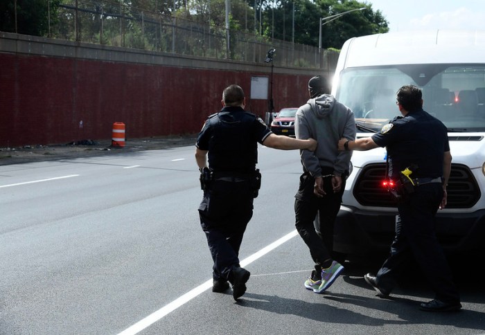 Cops snag 132 vehicles for "ghost plates" at NYC bridges 2 police arresting a man n NYC during a "ghost plates" operation