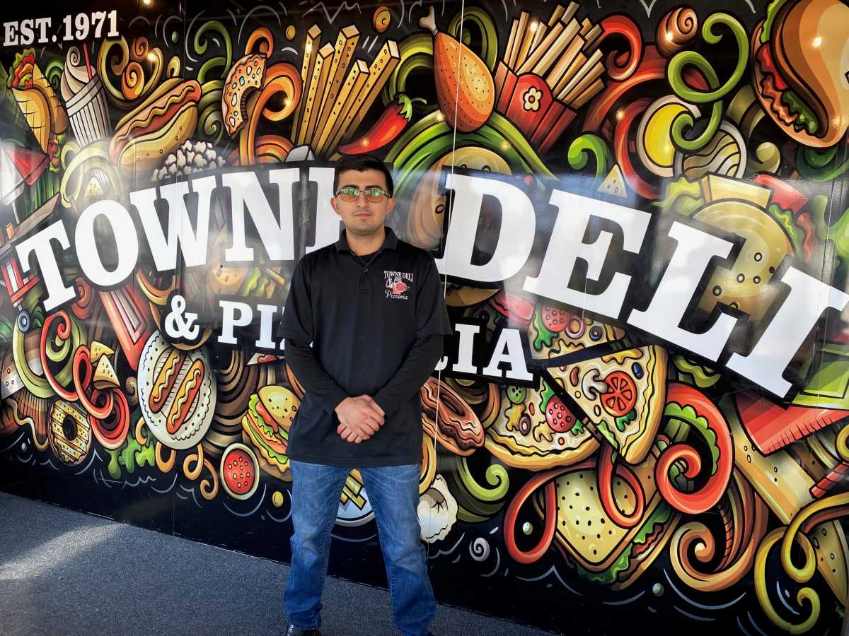 man in a black shirt standing in front of Towne Deli & Pizzeria sign on Staten Island