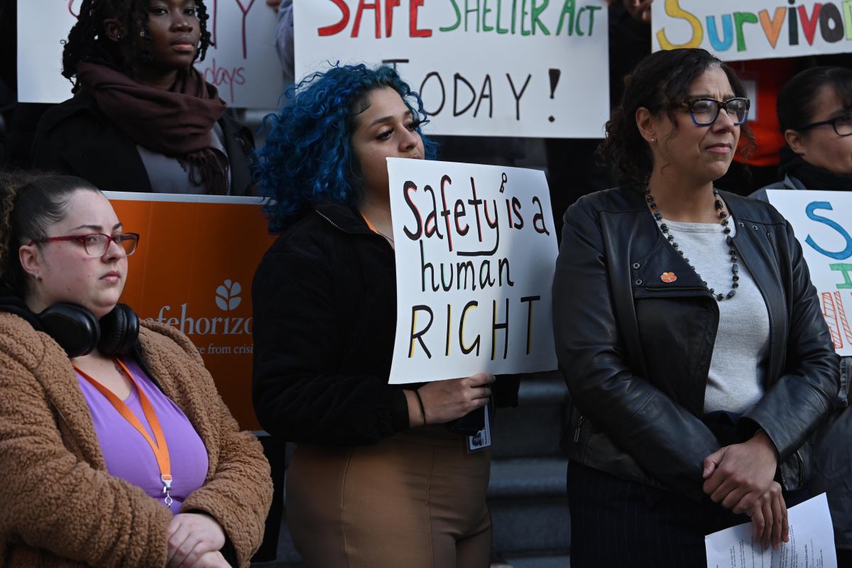 People holding signs reading messages for the passage of the Safe Shelter Act