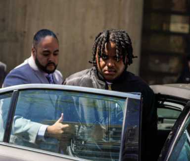 Suspect in Harlem grandmother's shooting with detective entering car during perp walk.
