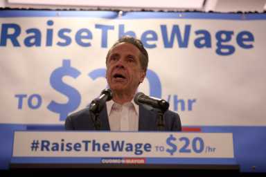 Former Gov. Andrew Cuomo speaking at podium about increasing minimum wage in NYC