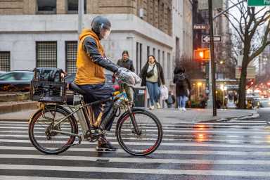 File image: Delivery man on an electric bicycle waiting for green traffic light - under new rules riders can be hit with criminal summons