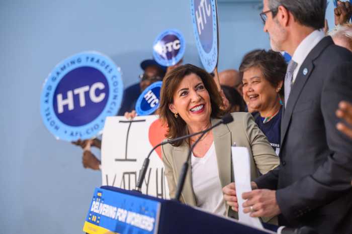 Woman smiling at podium as people hold union signs