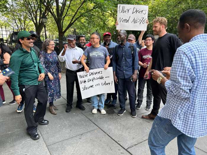 Uber and Lyft drivers standing on a sidewalk holding signs