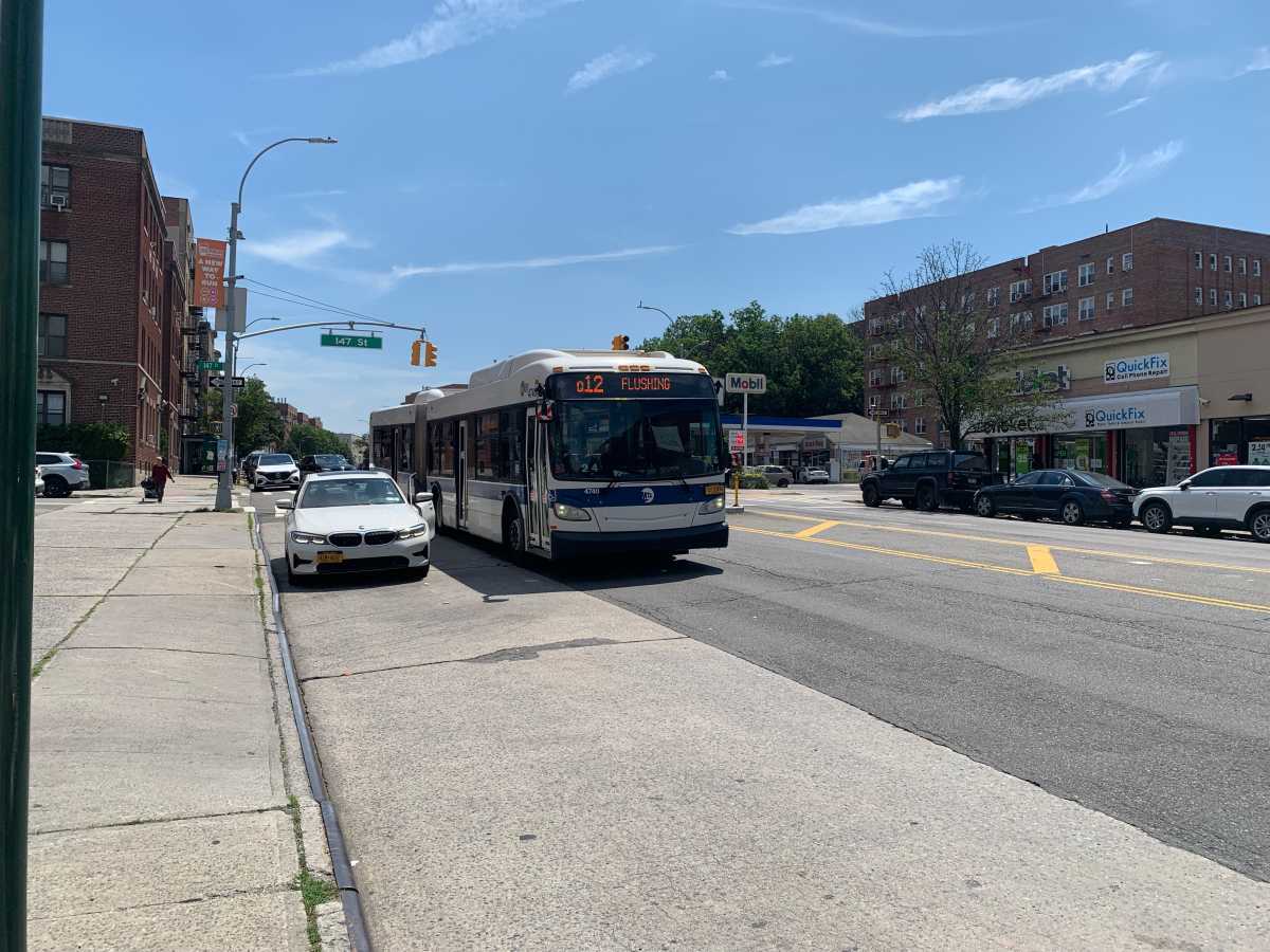 NYC bus arriving at a bus stop in Queens on a sunny day
