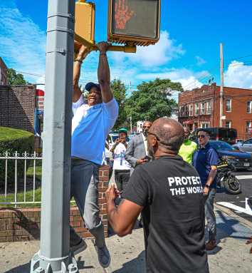 Man in white shirt doing pull-ups off of a Brooklyn street signal