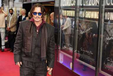 man with sunglasses, long hair and coat on red carpet.