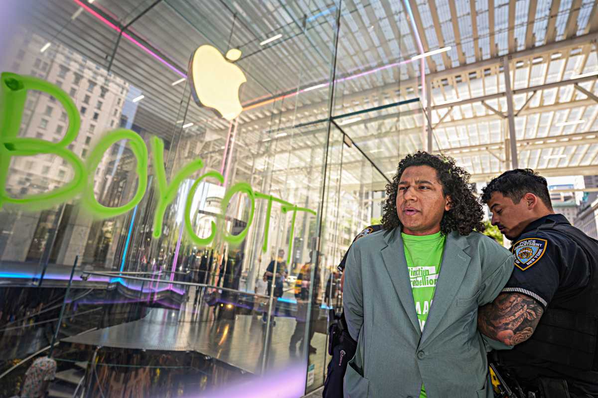 Man in green shirt arrested by police officer with word boycott spray-painted in green on Apple store window
