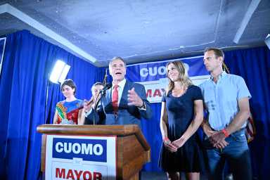 Man standing at podium with people speaking