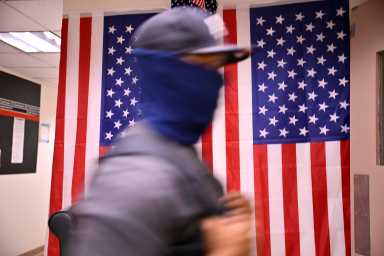 Man in mask walks past American flags at 26 Federal Plaza in NYC
