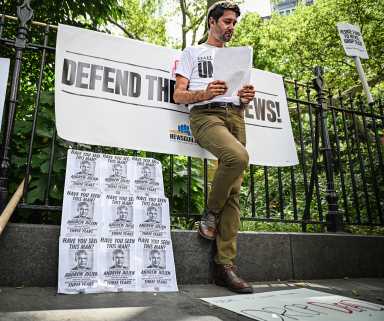 Daily News reporter stands against gate flanked by signs seeking reform