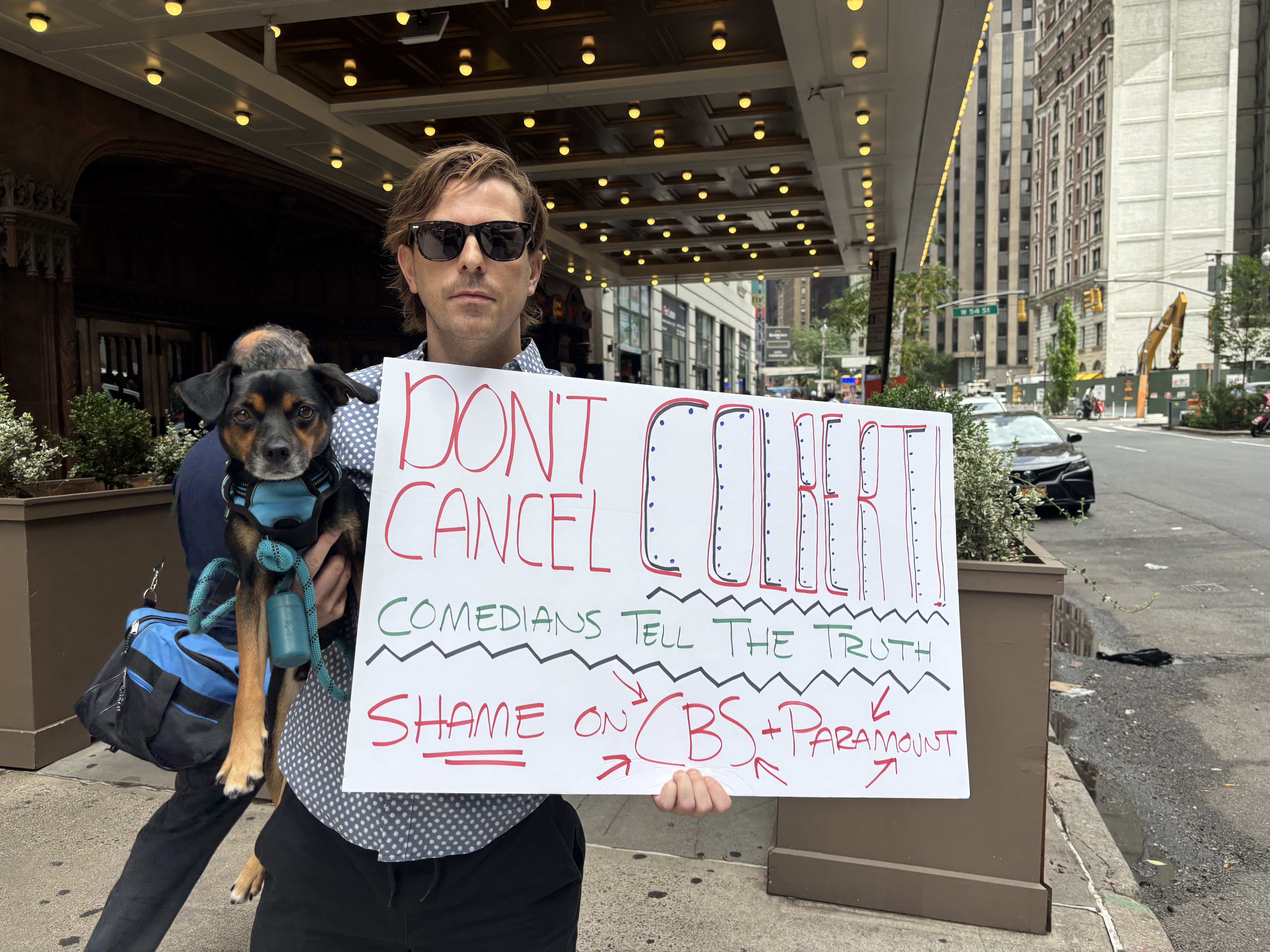 'Late Show' lament: For Midtown businesses, Stephen Colbert cancellation marks the end of an era 2 Man holds sign reading "DONT CANCEL COLBERT, COMEDIANS TELL THE TRUTH, SHAME ON CBS + PARAMOUNT" with his dog in front of "The Late Show" marquee.