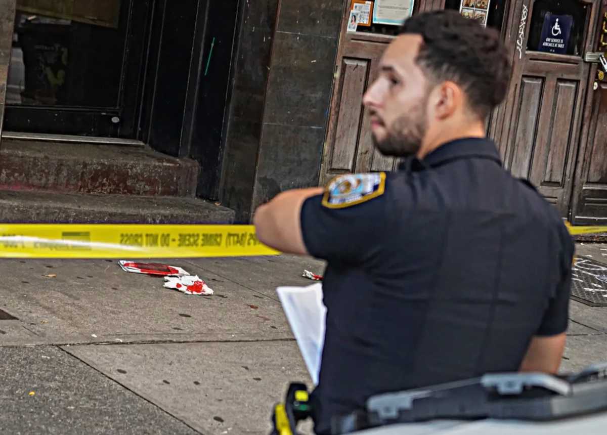 police officer with yellow tape at crime scene where person was stabbed with blood-covered cloth on ground
