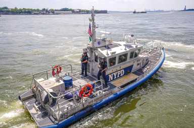 NYPD harbor boat with two officers on deck patrolling murky waters of East River