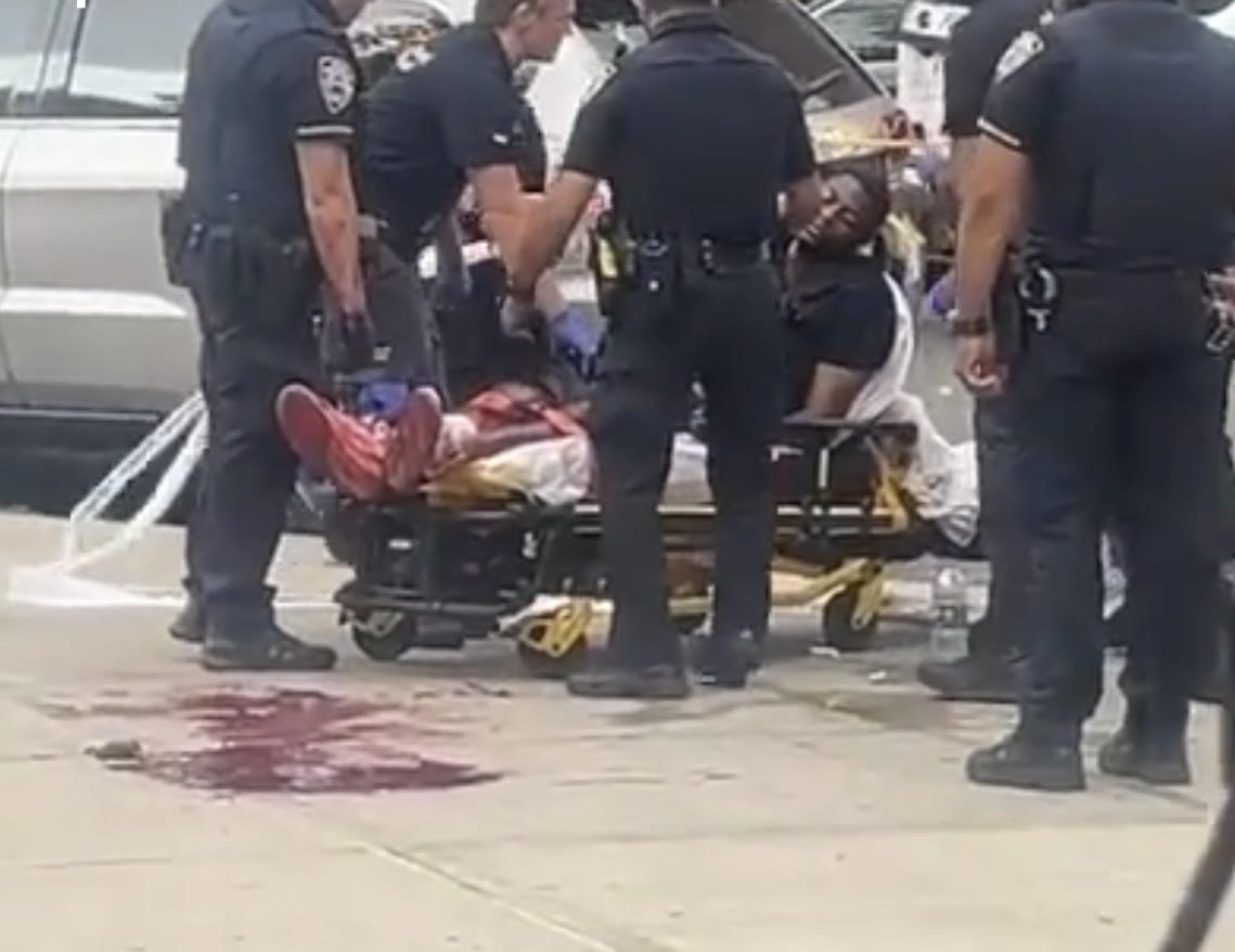 Police officers tend to shooting victim lying in pool of blood on gurney in Harlem