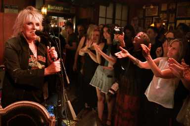 Lucinda Williams on stage, Johnny Cash in the bathroom at the East Village's newest honky-tonk bar 13 woman singing on stage as fans applaud at Lucinda's in East Village